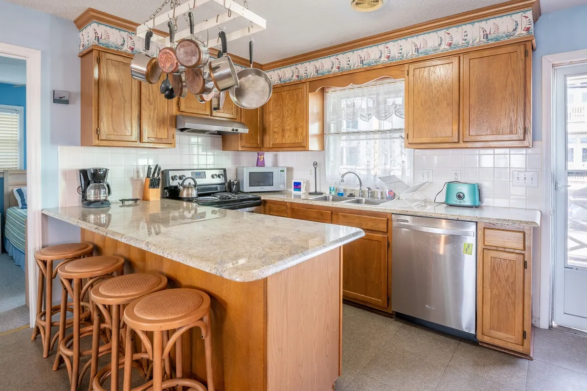 A homey kitchen with granite countertops, wooden cabinets, and hanging pots and pans. Kitchen appliances are visible, and the space feels ready for holiday cooking, family gatherings, and preparing fresh finds from the local farmer’s market.