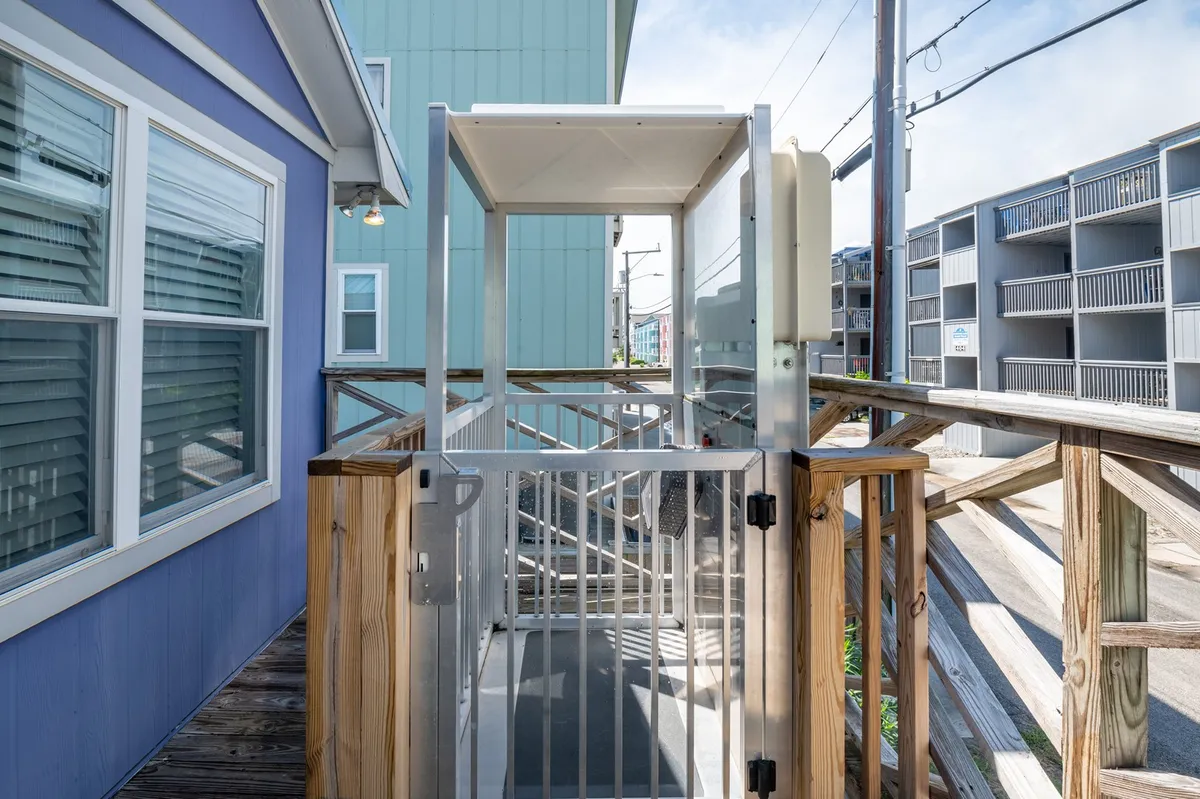 This exterior image showcases a wooden ramp with railing, blue siding, and a visible metal elevator structure adjacent to the house. The accessible path and elevator hint at ease of entry and thoughtful accommodations for various mobility needs.
