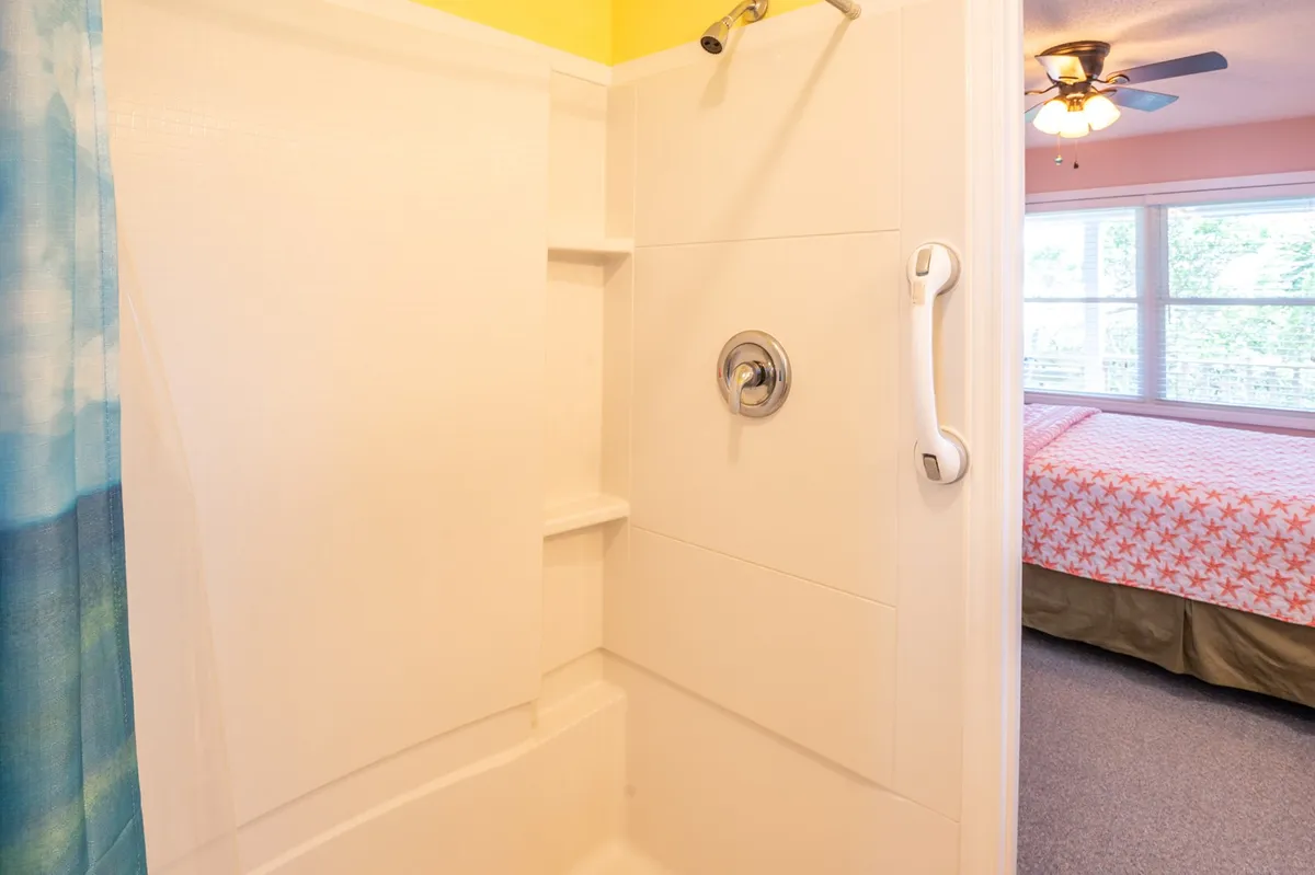 This interior image features a shower area with a colorful curtain and a view into a bedroom. The space is clean, bright, and practical, ideal for washing off sandy swimsuits or after a day at the beach.
