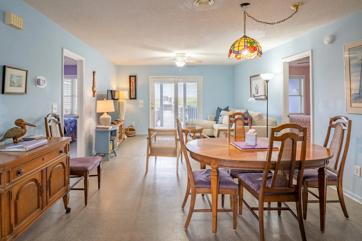 A spacious dining area with a central table under a chandelier, adjacent to a cozy sofa area and decorative accents. The scene exudes warmth and invites shared meals, celebrations, or family game sessions.