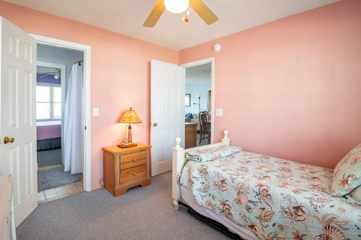 This inviting scene features a single bed with a floral quilt and a cozy nightstand with a lamp, while open doors connect to other rooms. The perspective hints at easy navigation and access between spaces, supporting a sense of connectivity suitable for guests of all ages.