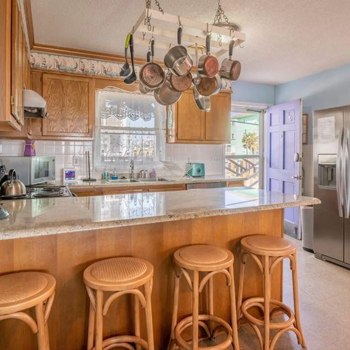 A welcoming kitchen space with a granite countertop, hanging pots, and bar stools. The open door hints at easy access to the outdoors, suggesting a lively spot for gathering before heading out to local events.